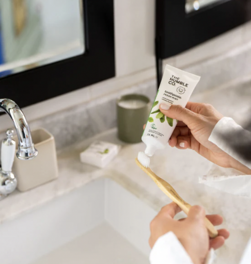 woman applying toothpaste to humble co toothbrush