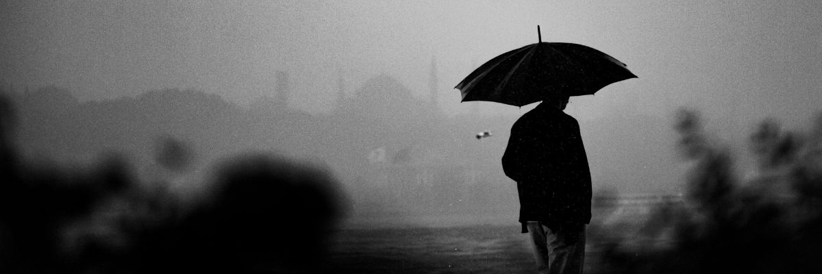 A black and white image of a person holding an umbrella walking in the rain.