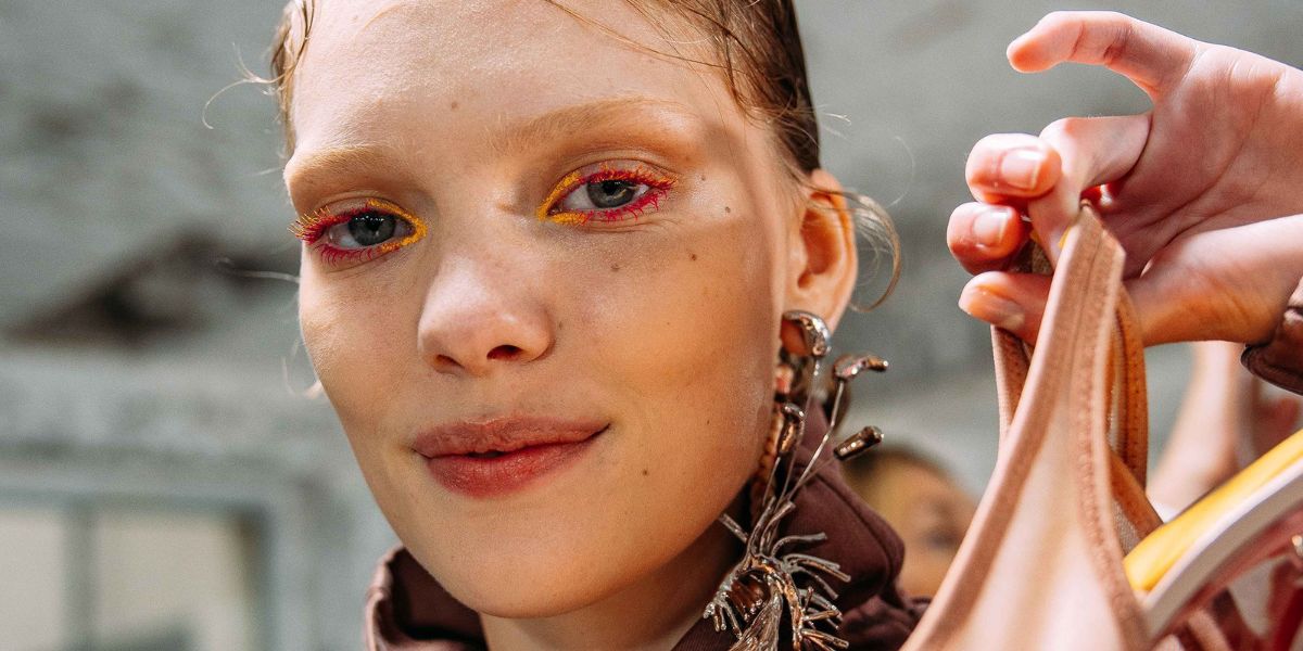 A model with orange and pink eye makeup poses at Fashion Week 2025 showing collection for Spring/Summer 2026.