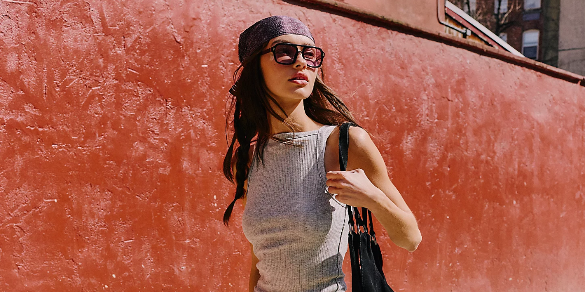 A woman stands in front of a red wall looking to the side holding a bag.